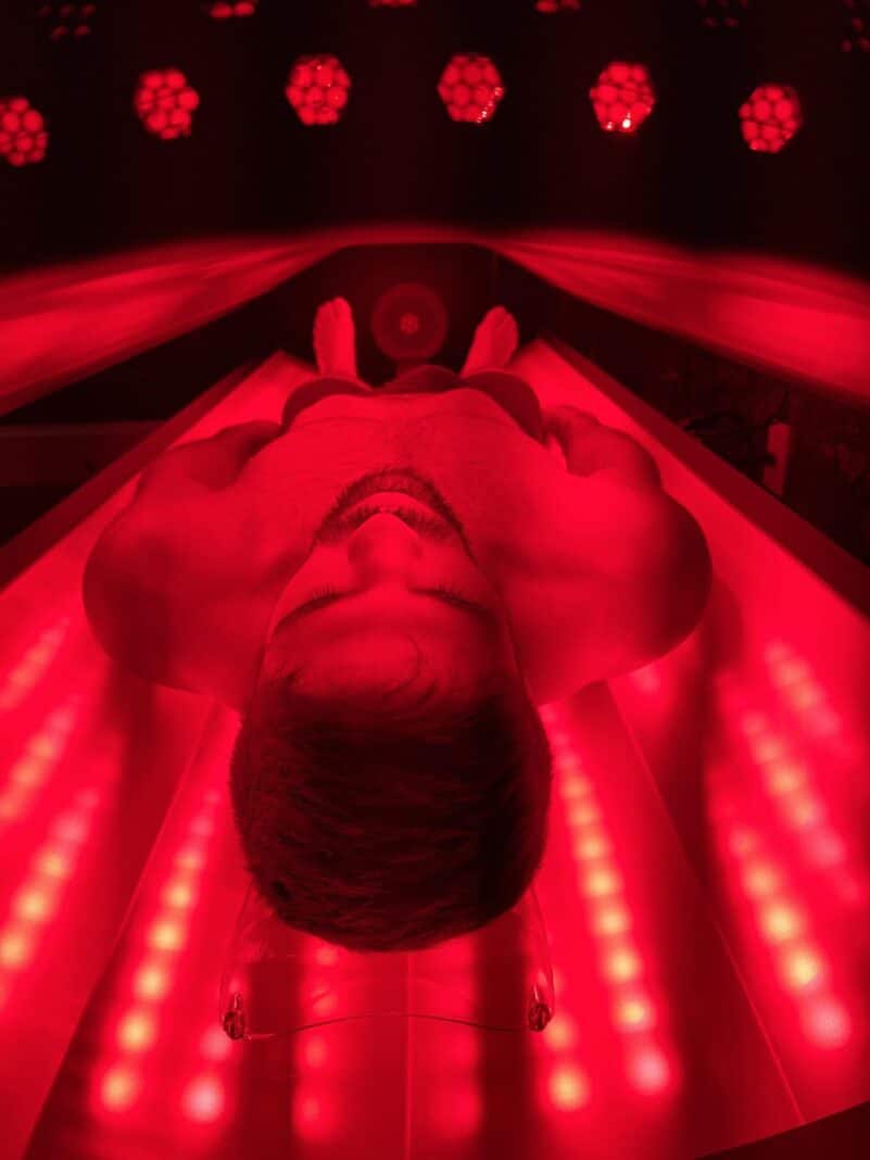 Patient inside the NovoTHOR whole-body red light therapy pod at Acupuncture Zen, Delray Beach, bathed in red and near-infrared light