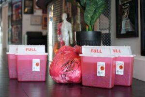 Full biohazard sharps containers and a red medical waste bag for used acupuncture needles at Acupuncture Zen in Delray Beach