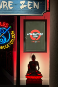 Acupuncture Zen clinic storefront on Atlantic Avenue Delray Beach Florida featuring illuminated sign Buddha statue and neon lighting at night