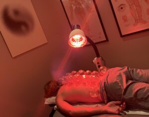 Patient receiving infrared heat lamp therapy over cupping treatment on their back with traditional Chinese medicine acupuncture charts on the wall at Acupuncture Zen Delray Beach FL