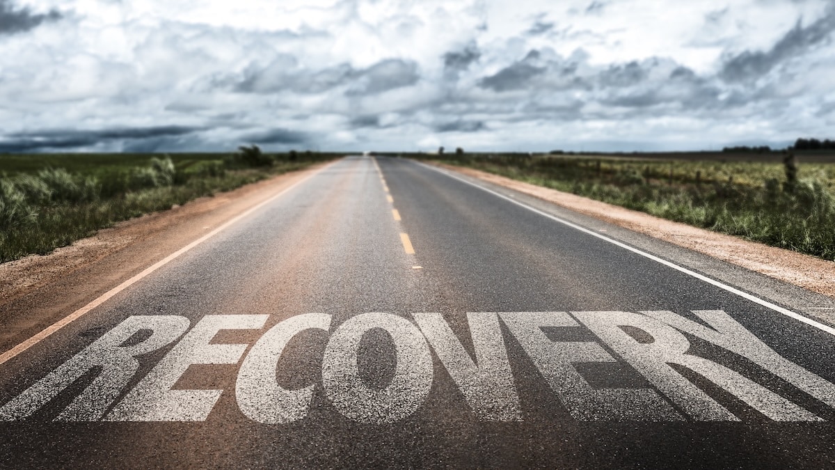 Open country road with the word "Recovery" painted on the asphalt, representing the path of addiction recovery