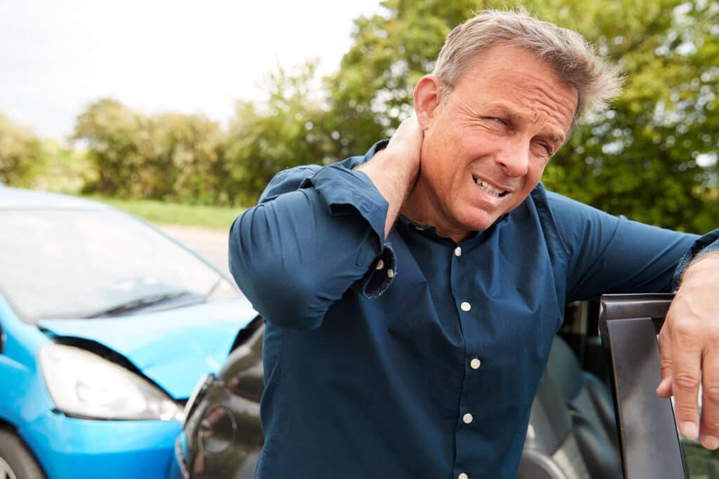 Man holding his neck in pain beside a crashed car after a whiplash injury