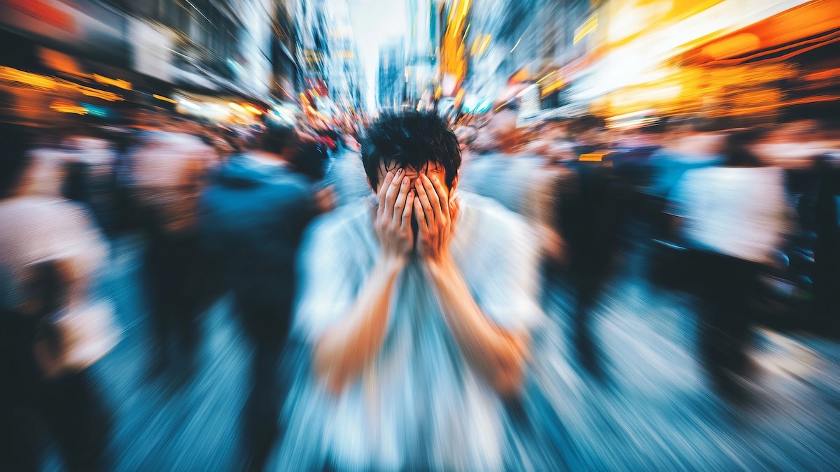 Young man is covering his face with his hands, feeling anxiety and fear in a very crowded street