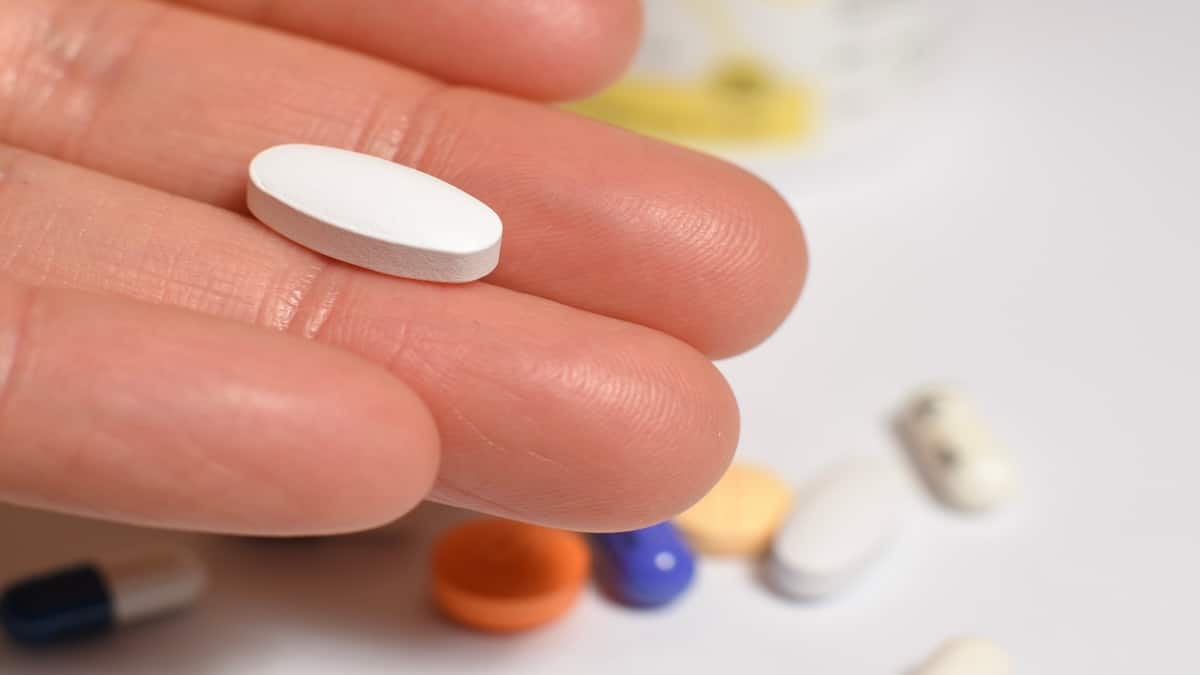 Hand holding a white pill with assorted medications in the background, representing chemotherapy side effects
