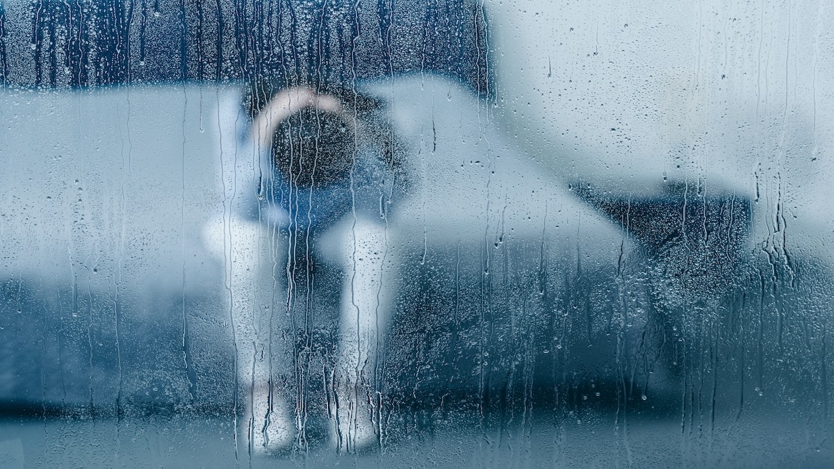 Person sitting hunched over, seen through a rain-streaked window, representing depression