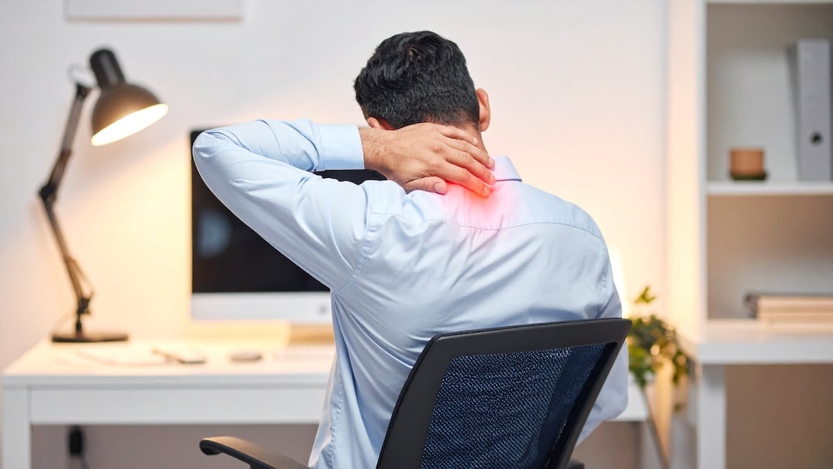 Man at an office desk holding the back of his neck with the area glowing red in pain, pain relief acupuncture in Delray Beach