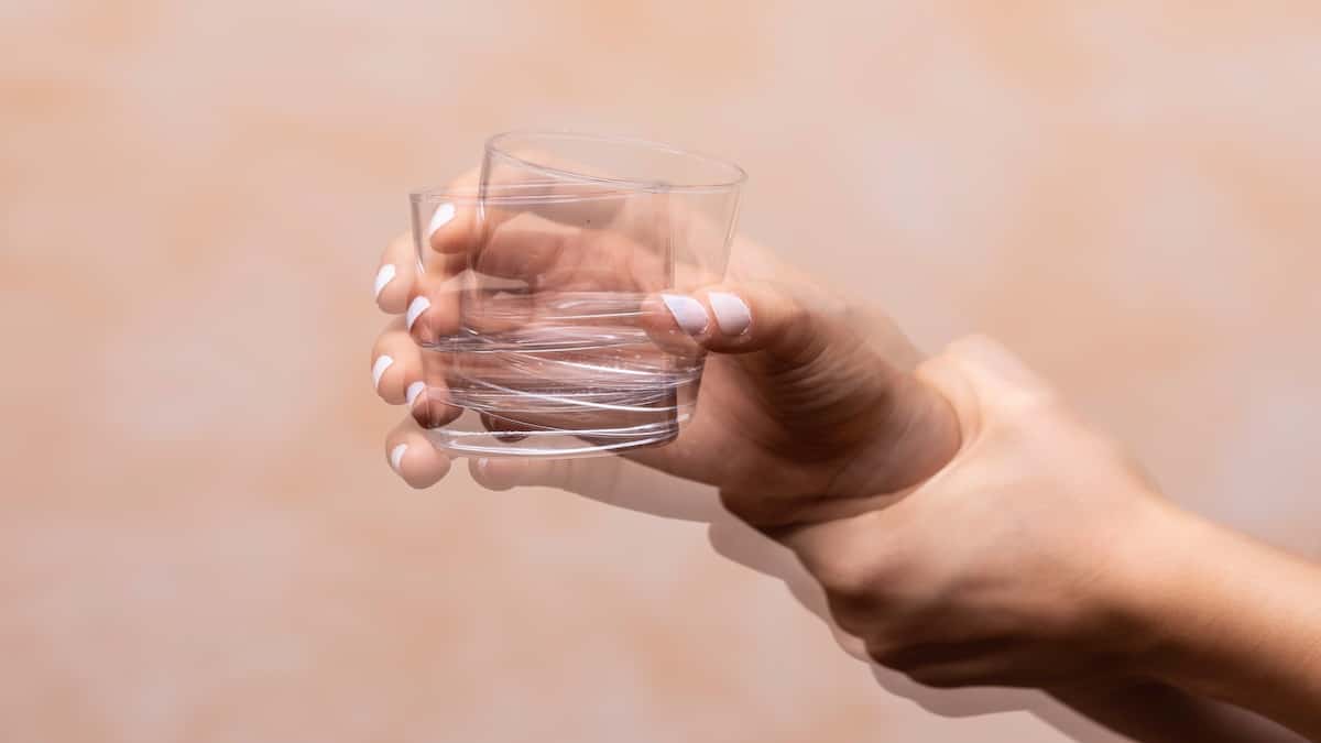 Person's hands steadying a glass of water showing a visible tremor, Parkinson's disease acupuncture in Delray Beach