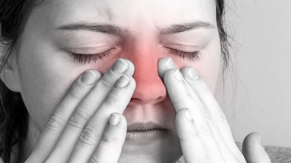 Woman pressing both sides of her nose with the sinus area tinted red to show congestion and pain, sinusitis acupuncture in Delray Beach