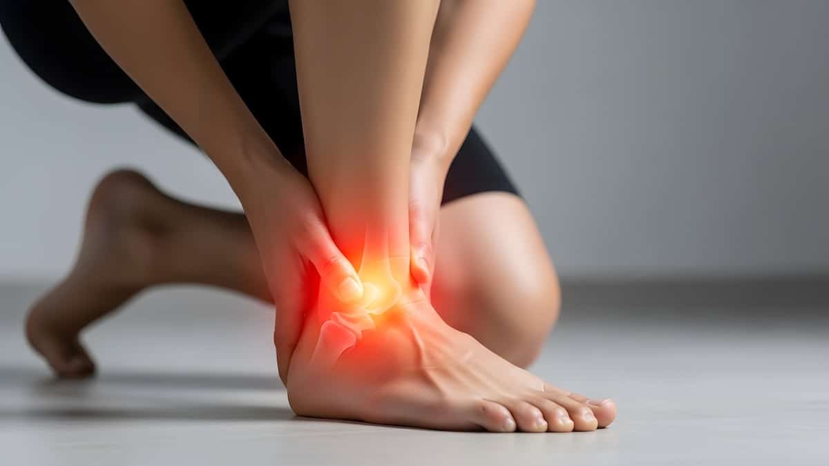 Person kneeling and holding a bare ankle with the joint glowing red and orange to show a sprain, sprain acupuncture in Delray Beach