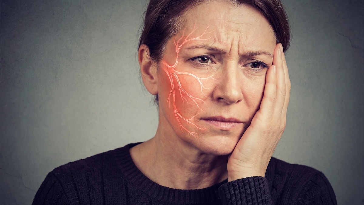 Woman holding her cheek in pain with the facial nerve pathways highlighted in red down one side of her face, trigeminal neuralgia acupuncture in Delray Beach
