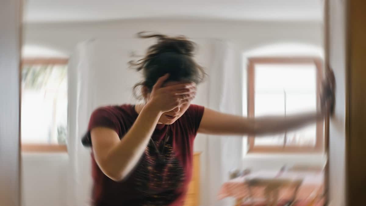 Woman steadying herself with a hand to her head in a blurred, spinning room conveying dizziness, vertigo acupuncture in Delray Beach