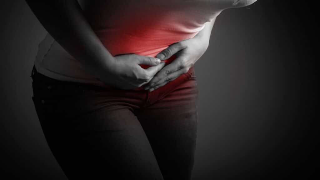 Woman holding her lower abdomen with pelvic pain highlighted in red, a common sign of endometriosis.